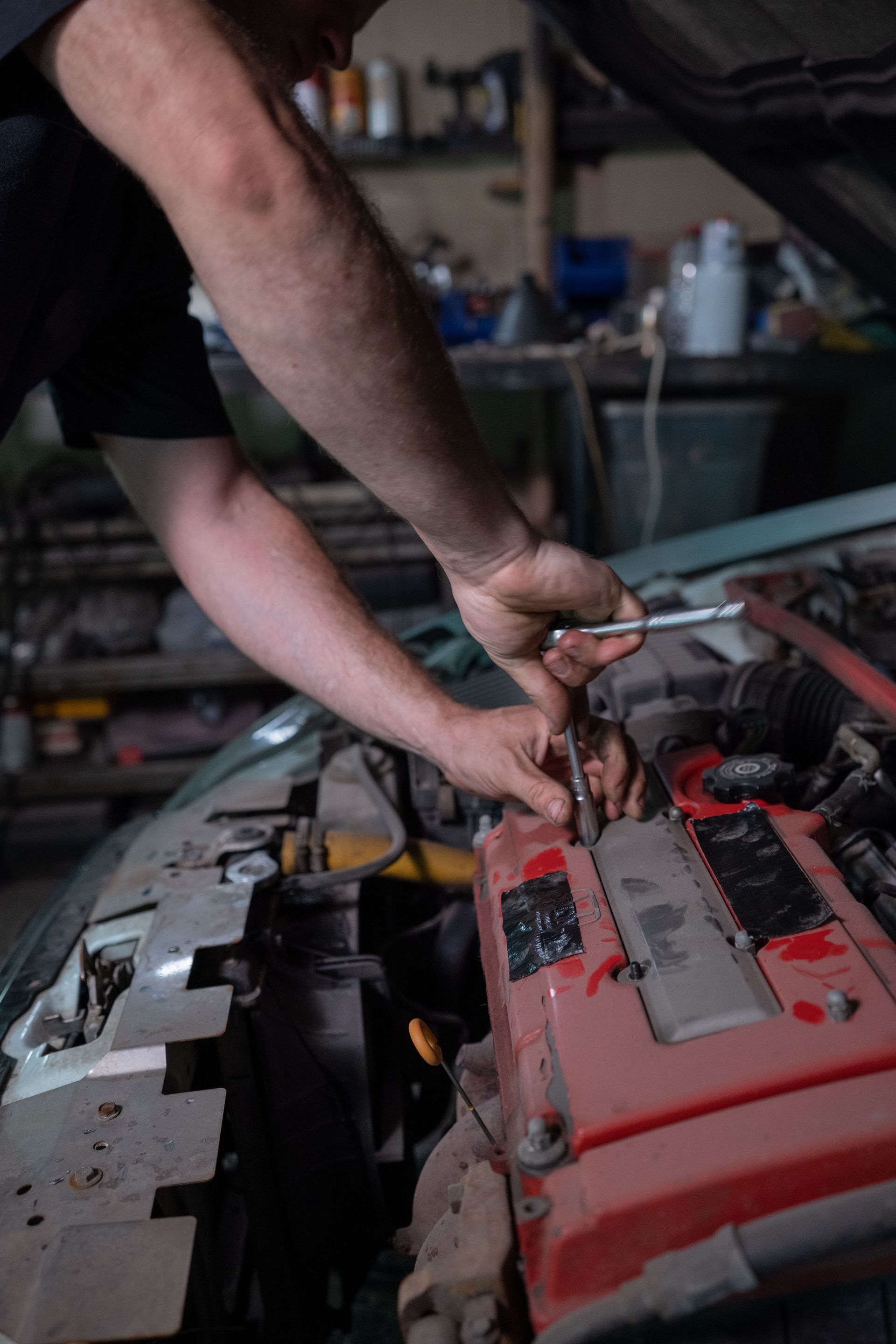 Mechanic repairs car engine in a dimly lit auto garage, focused on fixing the vehicle.